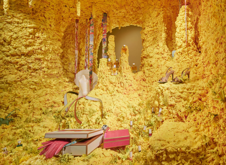 Escaparate veraniego de Hermès con frutas tropicales y vegetación exuberante en tonos vibrantes, transmitiendo frescura y color para el retail de verano.