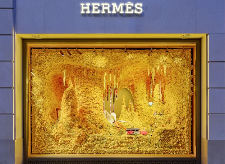 Instalación veraniega de Hermès con referencias al trópico y materiales naturales en un escaparate vibrante y llamativo.