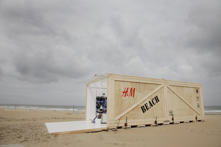 Pop-up de H&M en la playa con estructura de madera clara, diseño minimalista y concepto abierto frente al mar.